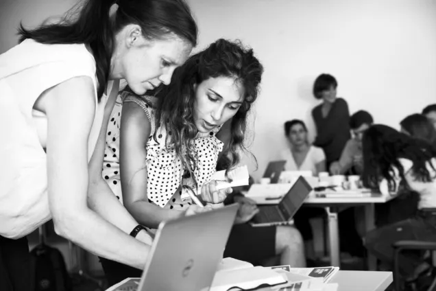 Two female students are chatting by a laptop. Photo.
