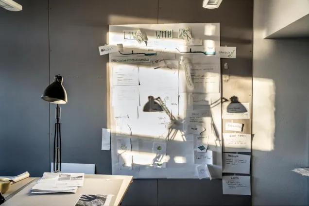 Arbetsplats med välfylld anslagstavla på väggen. Foto.