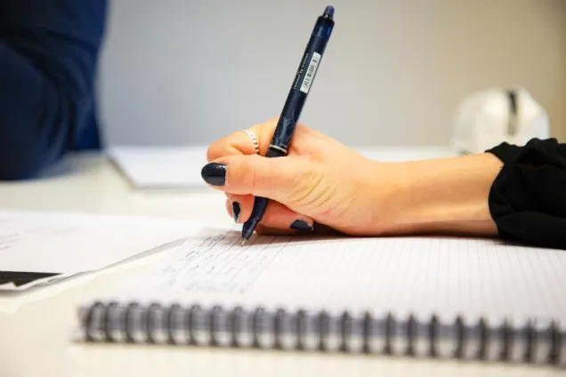 Närbild på en kvinnlig hand som skriver i ett block. Foto.