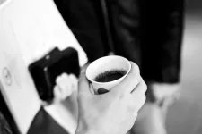 Händer som håller i kaffemugg och bibba med papper. Foto.