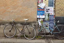 Två cyklar står parkerade vid husvägg. Foto.