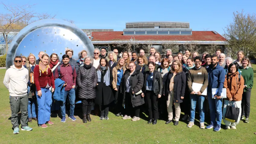 Grupp människor står framför metallskulptur och konferenslokal. Foto.